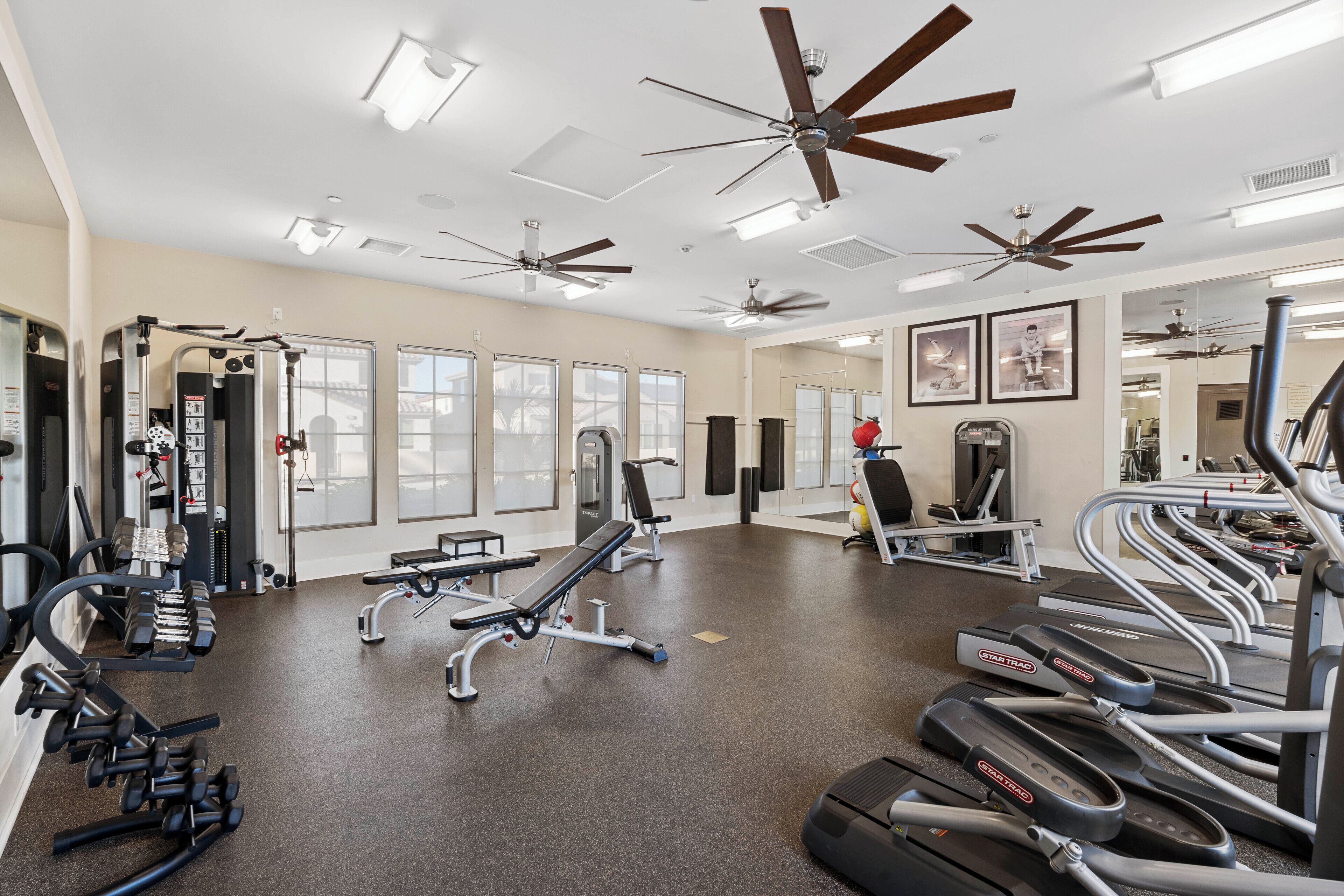 A gym with treadmills, weight machines, and ceiling fans.