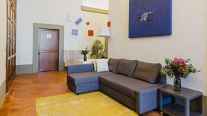 A living room with a sectional sofa, a small table with a vase, and a painting on the wall.