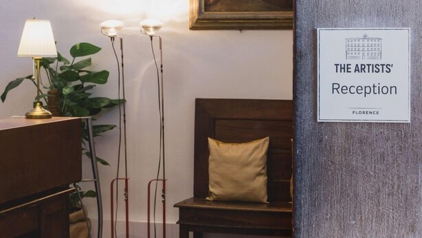 A reception area with a framed painting, a lamp, and a sign reading "THE ARTISTS' Reception Florence".