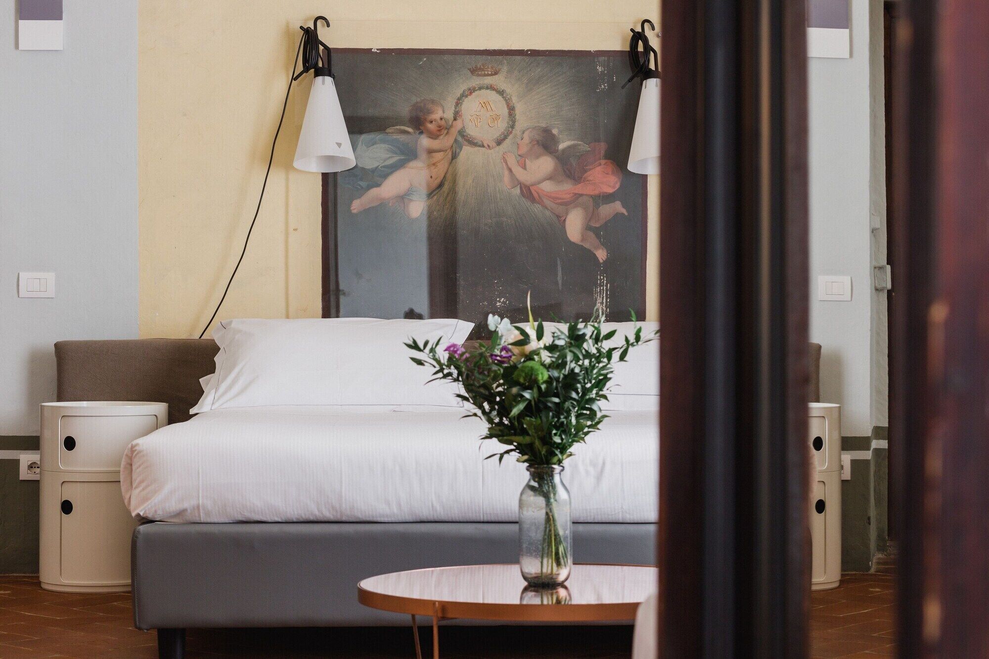 A bedroom with a bed, bedside tables, a nightstand, a vase with flowers, and a painting on the wall.