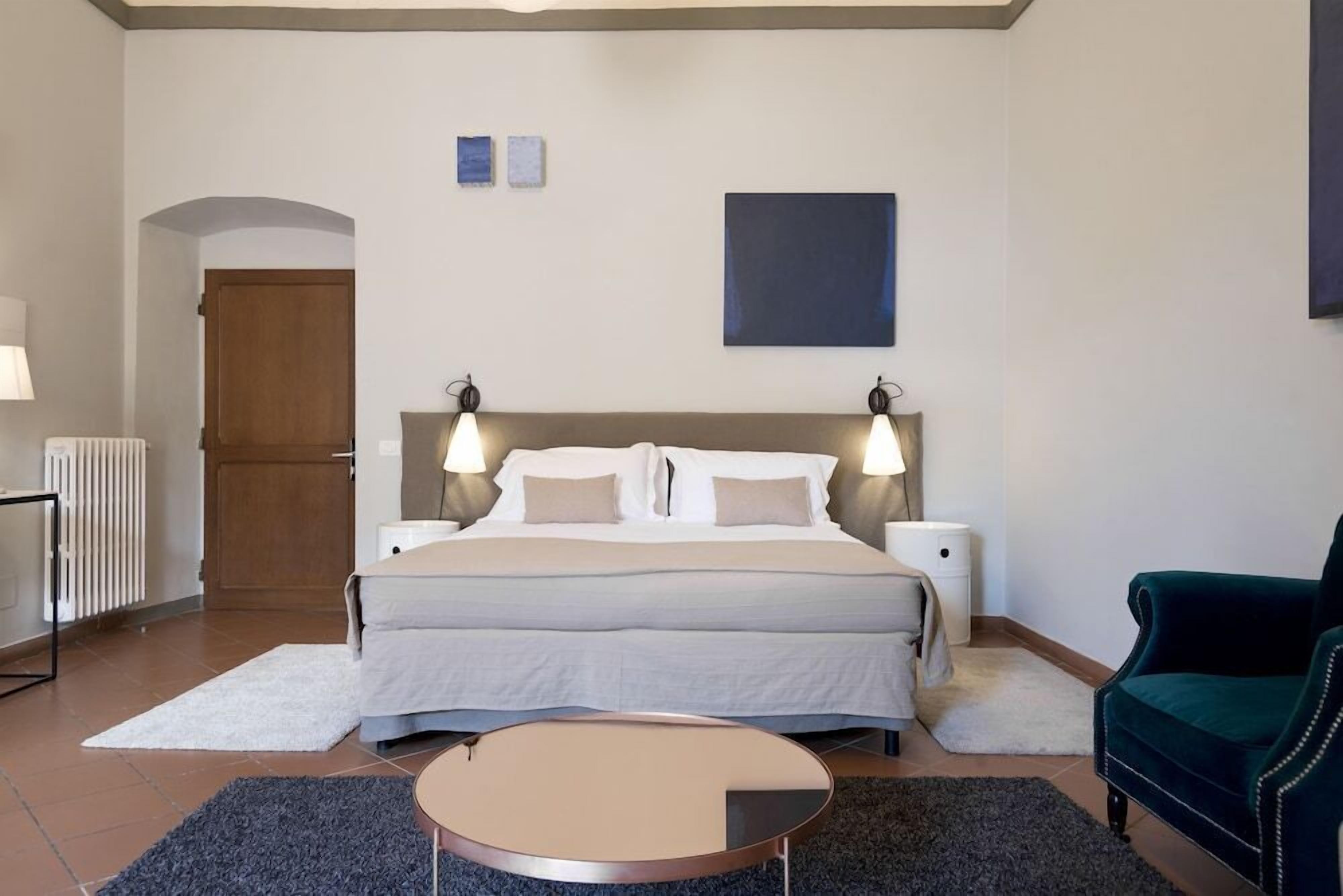 A bedroom with a bed, bedside lamps, a round table, a chair, and a radiator.