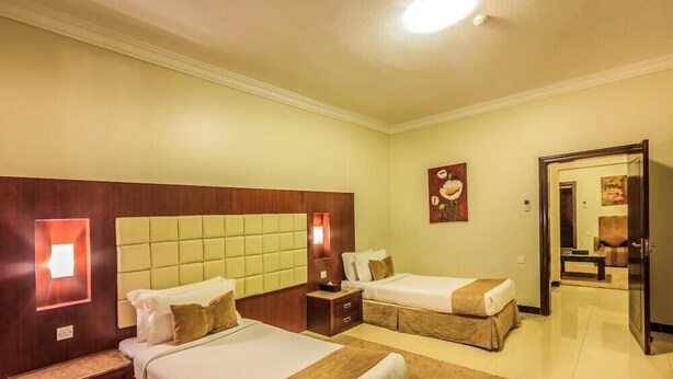 A hotel room with two beds, a wooden headboard, a nightstand, a mirror, and a door leading to another room. - Almuhaidb King Abdul Aziz (Riyadh)