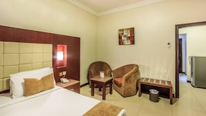 A hotel room with a bed, two chairs, a small table, a trash bin, and a painting on the wall. - Almuhaidb King Abdul Aziz (Riyadh)