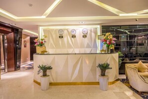 Um balcão de recepção com relógios, plantas em vasos e uma área de estar com um sofá e poltronas.