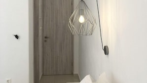 A hallway with a wooden door, a hanging geometric light fixture, and a bed with white bedding. - Studios Taki's Place (Naxos)
