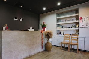 A reception area with a reception desk, a large vase with dried plants, wooden chairs, and shelves with framed pictures. - Go Walk Jiufen (New Taipei City)