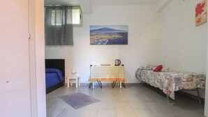 A small, well-lit room with a bed, a small table with a kettle, and a framed picture of a mountain on the wall. - Catania Aeroporto (Catania)