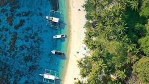 An aerial view of a beach with several boats docked along the shore, surrounded by dense palm trees. - Villa Israel Ecopark El Nido by Cocotel Powered by Fave (El Nido)