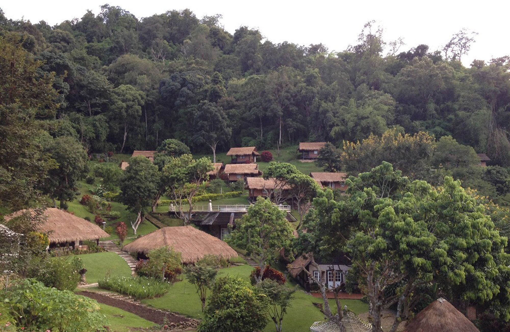 A rural village with thatched-roof houses surrounded by lush greenery and hills.