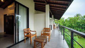 A covered balcony with wooden furniture, a sliding glass door, and a view of greenery.