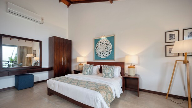A bedroom with a large bed, a wooden wardrobe, a mirror, a painting, and a lamp. - Mirissa Beach Villa (Thalaramba)
