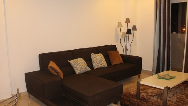A modern living room with a dark brown sectional sofa, patterned cushions, a small white coffee table, and a shaggy rug.