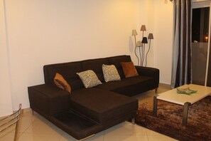A modern living room with a dark brown sectional sofa, patterned cushions, a small white coffee table, and a shaggy rug. - Accra Luxury Apartments (Accra)