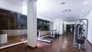 A spacious gym with exercise equipment, large windows, and a wooden floor.