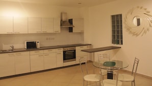 A modern kitchen with white cabinets, a microwave, an oven, and a dining area with a glass table and chairs.