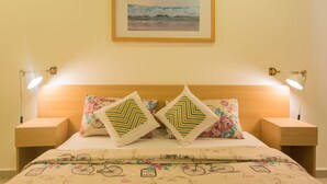 A neatly made bed with floral and geometric patterned pillows, a Paris-themed duvet, and a framed seascape above it.