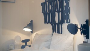 A bedroom with a bed, white pillows, a bedside table with a lamp, a mirror, and a wall art piece. - Suite Garibaldi Cosy Design Lyon Centre (Lyon)
