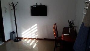 A room with a coat rack, a flat-screen TV mounted on the wall, a small table with a vase, and a chair. - Haoxin Hotel (Accra)