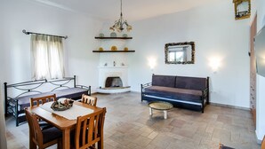 A room with a dining table, chairs, a sofa, a fireplace, a chandelier, and a mirror. - Anemonisia (Skiros)