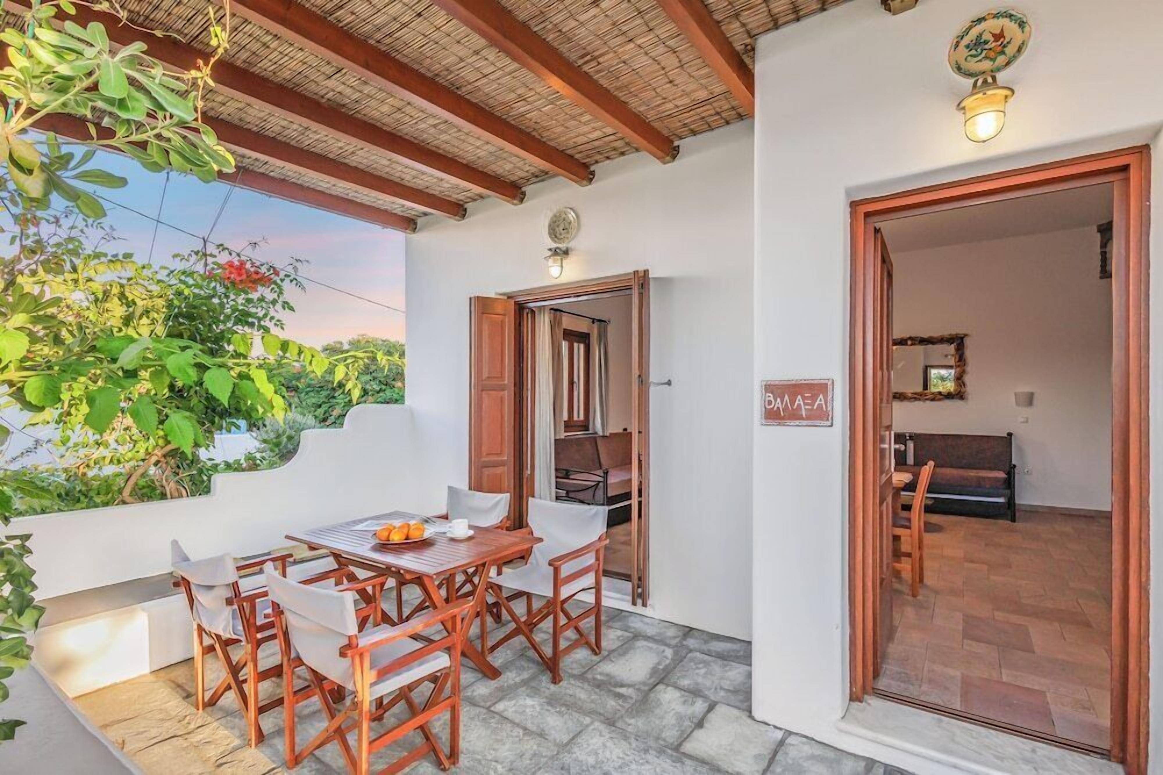Un patio al aire libre con una mesa y sillas, techo de madera y una puerta que da a una habitación interior.