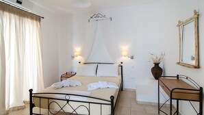 A bedroom with a bed, bedside tables, a mirror, and a window with curtains. - Anemonisia (Skiros)