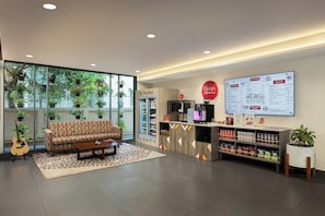 Eine moderne Lobby mit einer Couch, einer Kaffeestation, einer Speisekarte und einem Kühlschrank.