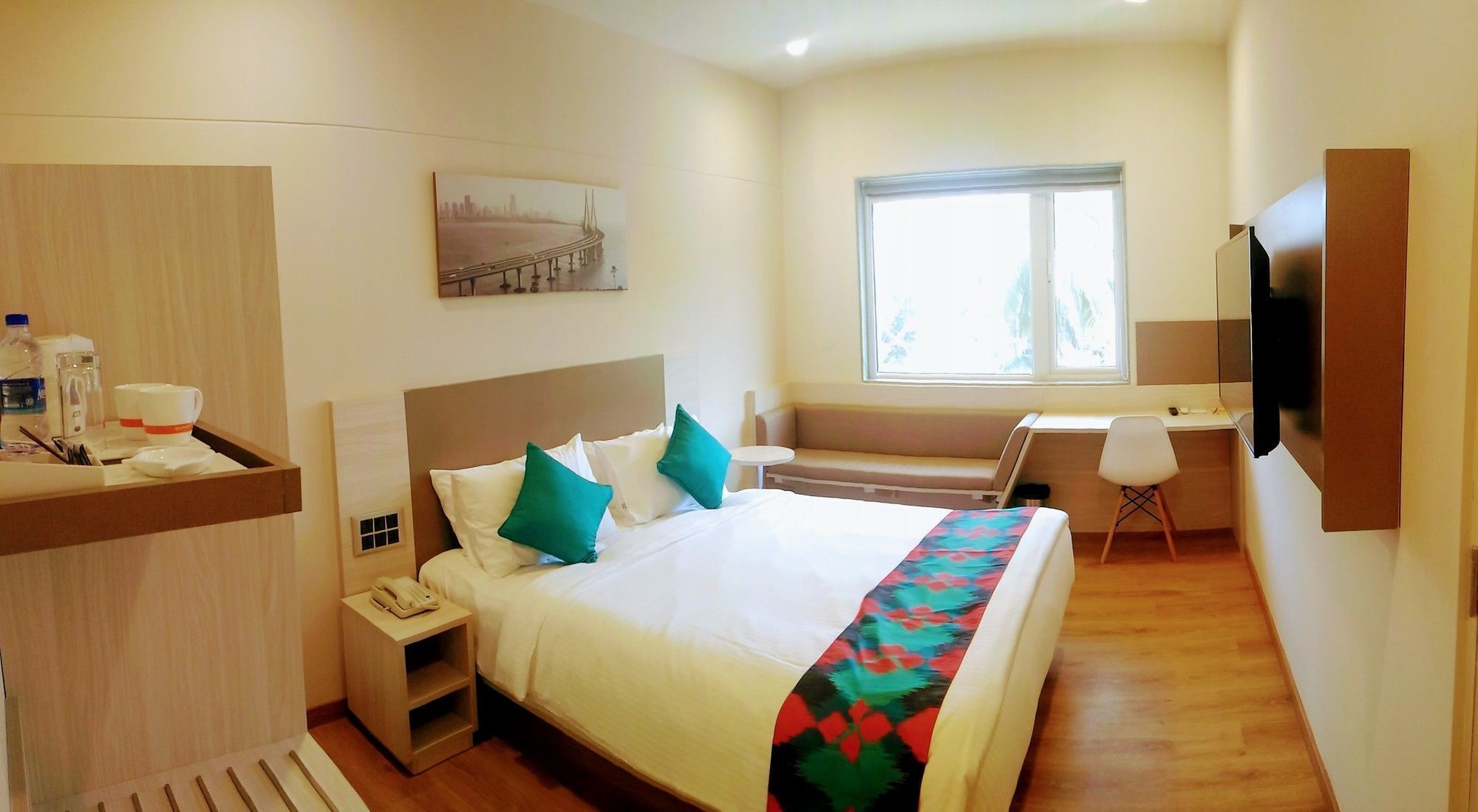 A hotel room with a bed, bedside table, a desk, a chair, a TV, and a window.