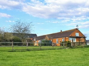 A rural house with a fenced yard, a car, and a clear sky.