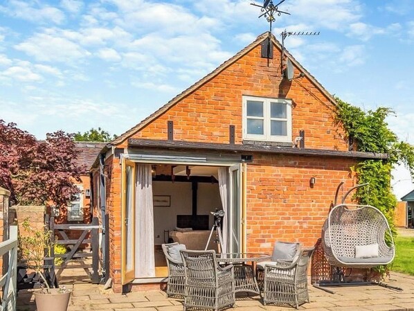 A brick house with a patio, wicker furniture, and a hanging chair.