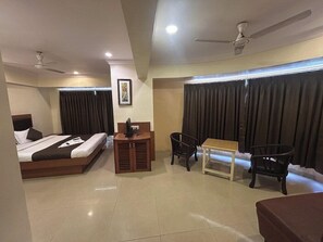 A hotel room with a bed, a desk, two chairs, a table, and a ceiling fan. - Hotel Lucky (Mumbai)