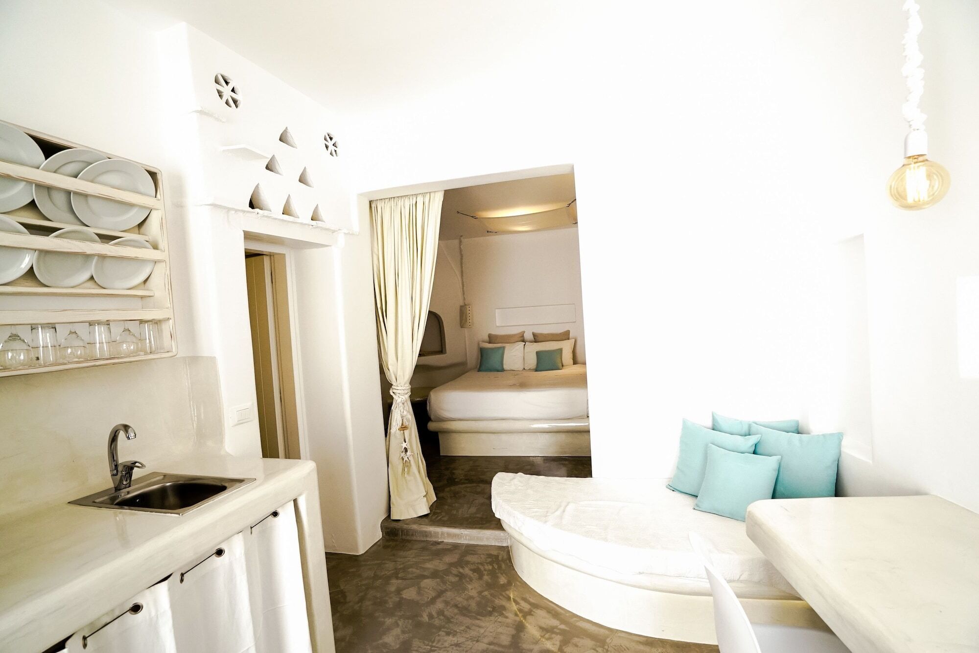 A compact, well-lit room with a bed, a small seating area, and a kitchenette.