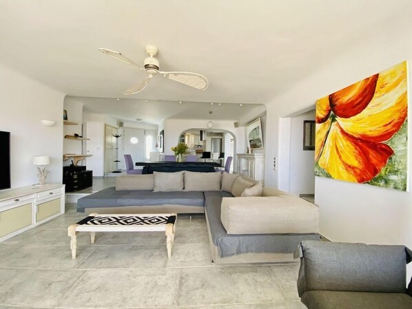 A modern living room with a sectional sofa, a coffee table, and a ceiling fan. - Flaskos Suites (Mykonos)