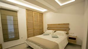 Ein Schlafzimmer mit Bett, Nachttischen, einem Holzkopfende, einem Fenster mit Jalousien und einer Klimaanlage.