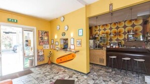 Vestíbulo de hotel con piso de baldosas de piedra, una recepción, una zona de bar con taburetes y un reloj en la pared.