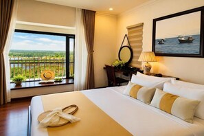 A hotel room with a bed, a window with curtains, a desk with a lamp, a framed picture, and a view of the outdoors. - Happy Life Memories Hoi An Hotel & Spa (Hoi An)