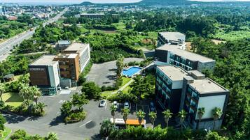 An aerial view of a modern hotel complex with multiple buildings, a swimming pool, and surrounding greenery.