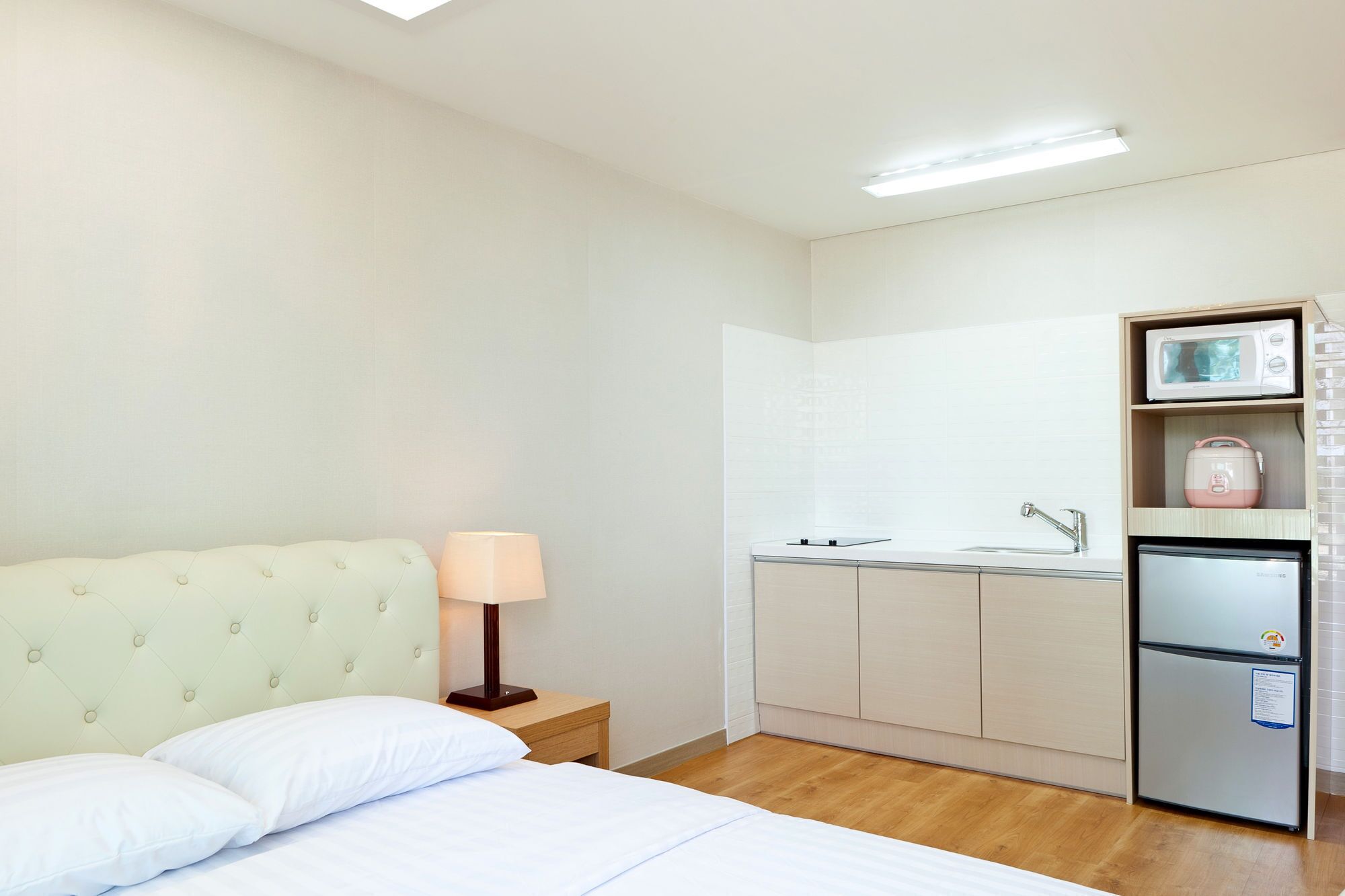 Une chambre d’hôtel compacte comprenant un lit, une lampe de chevet, une kitchenette avec un réfrigérateur et un four à micro-ondes.