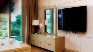 Een moderne hotelkamer met een houten vloer, een beige dressoir met lades, een grote spiegel, een flatscreen televisie aan de muur en een raam met gordijnen.
