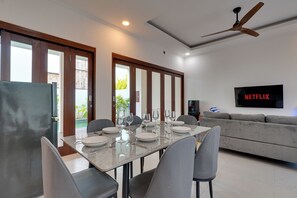 Un comedor moderno con una mesa preparada para cuatro personas, un sofá y un televisor con el logotipo de Netflix.