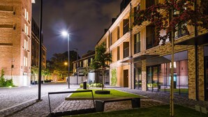 A courtyard with a paved walkway, a bench, and a small garden area with a tree and plants. - Exclusive Apartments (Kraków)