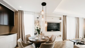 A modern dining area with a round table, four chairs, a vase of flowers, and a flat-screen TV mounted on the wall. - Exclusive Apartments (Kraków)