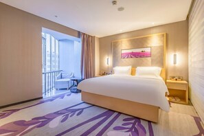 Ein Hotelzimmer mit einem großen Bett, einem Nachttisch, einem Beistelltisch, einem Sessel und Blick auf die Stadt.
