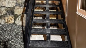 A wooden exterior staircase leading to a building with a stone wall and a metal railing. - Luxury 2-Bedroom Suite at Bear Mountain | Victoria (Langford)