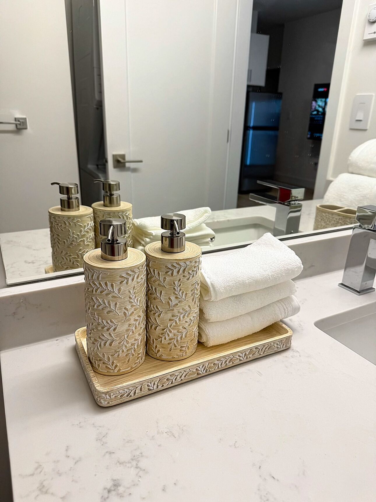 Un tocador de baño con encimera de mármol, un espejo grande y tres dispensadores decorativos para jabón.