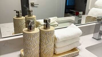 Un tocador de baño con encimera de mármol, un espejo grande y tres dispensadores decorativos para jabón.