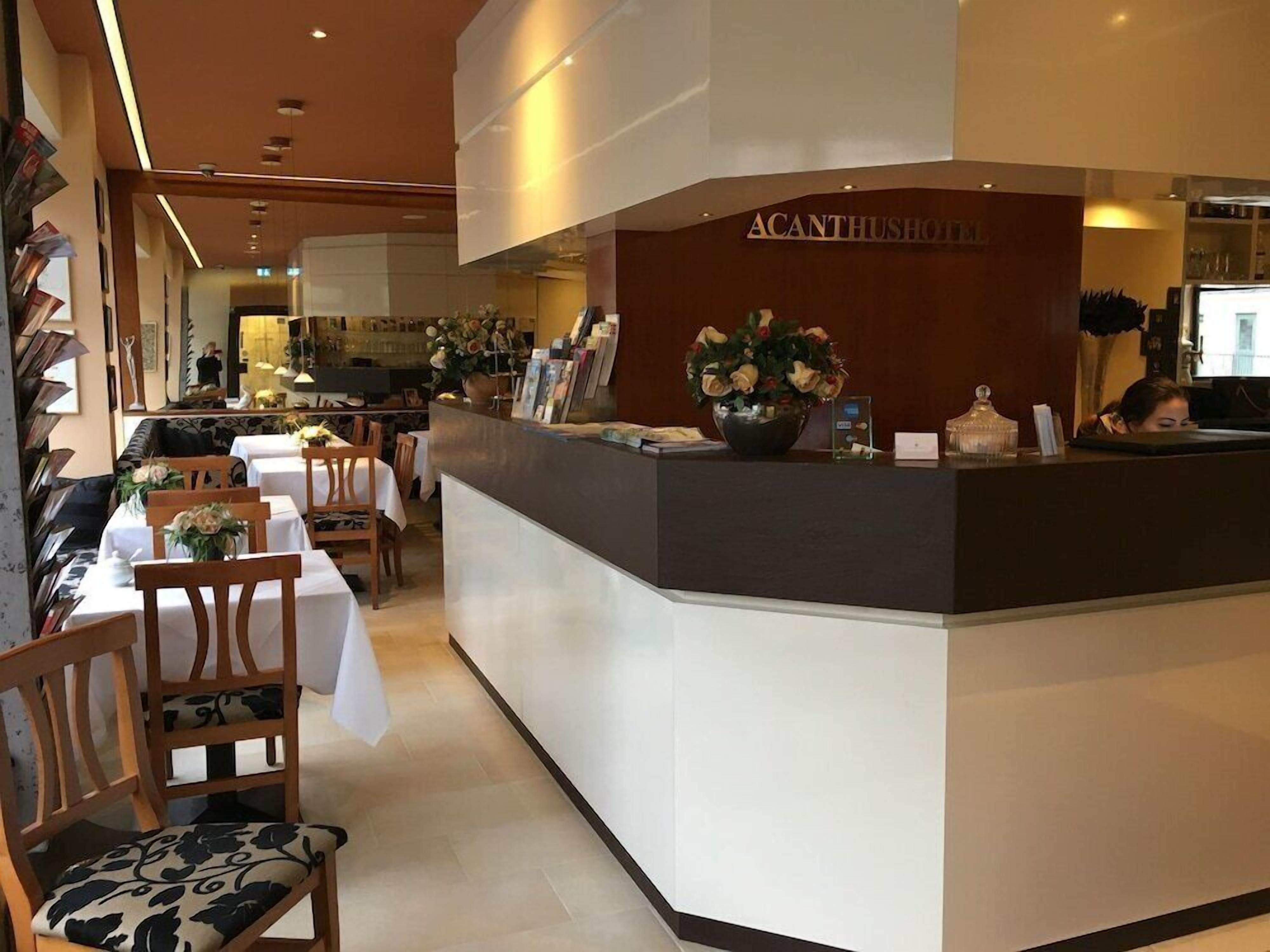 Ein Hotel-Rezeptionsbereich mit Theke, Stühlen, Tischen und einer Blumenvase.