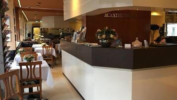 Ein Hotel-Rezeptionsbereich mit Theke, Stühlen, Tischen und einer Blumenvase.