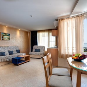 A modern living room with a sofa, armchair, and dining table with fruit. - Blue Bay Hotel (Nessebar)