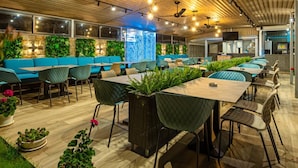 A modern restaurant with wooden ceiling, green plants, and blue seating. - Blue Bay Hotel (Nessebar)