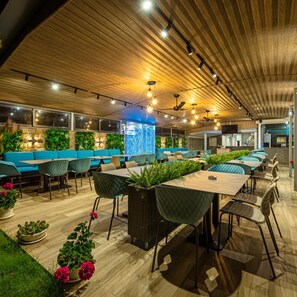 Un restaurant modern amb sostre de fusta, plantes verdes i seients blaus.